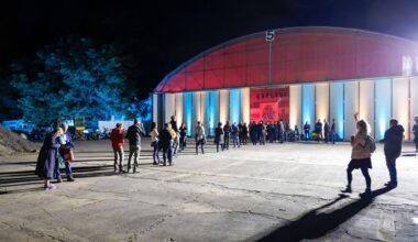 Menschen warten vor einer Halle auf Einlass.
