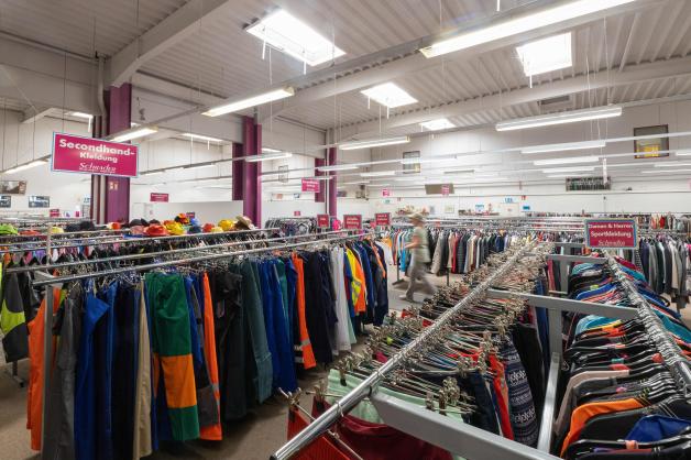 Arbeitshosen und Hemden für Männer, Kinder- und Damenkleidung hängen im Secondhand-Laden von Schrader.
