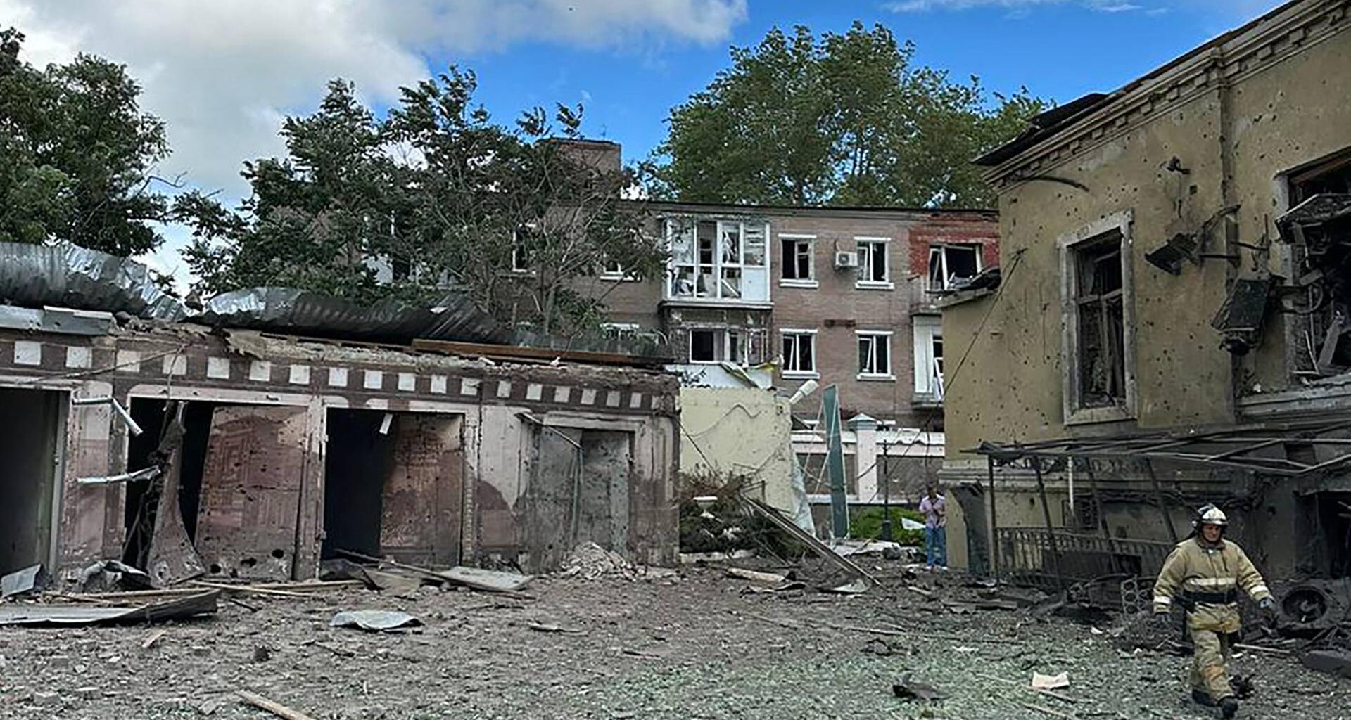 Das Foto zeigt mehrere zerstörte Gebäude. Ein Feuerwehrmann läuft über den Platz davor.