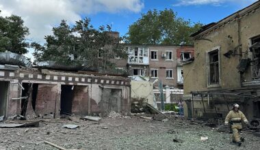 Das Foto zeigt mehrere zerstörte Gebäude. Ein Feuerwehrmann läuft über den Platz davor.