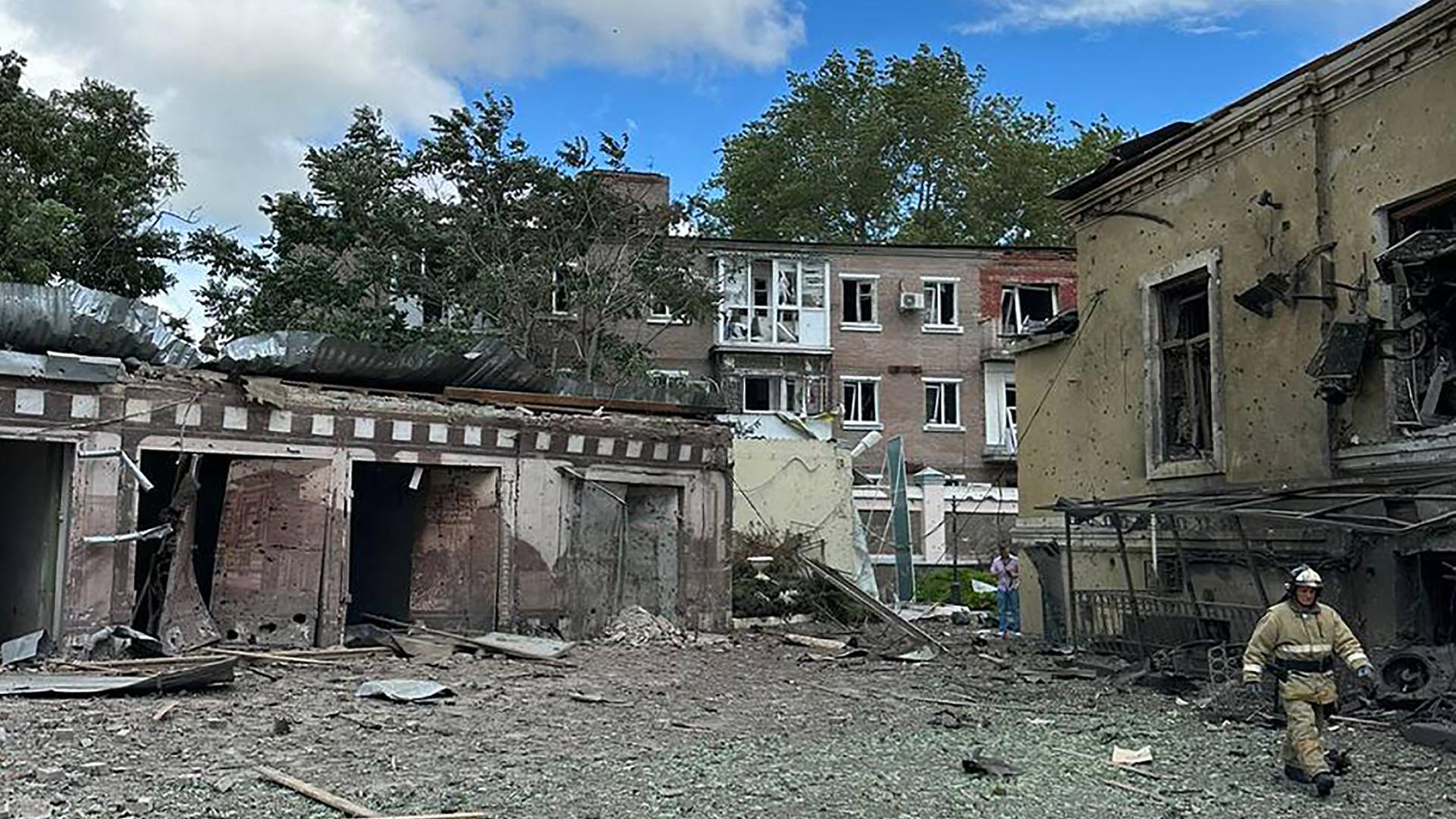 Das Foto zeigt mehrere zerstörte Gebäude. Ein Feuerwehrmann läuft über den Platz davor.