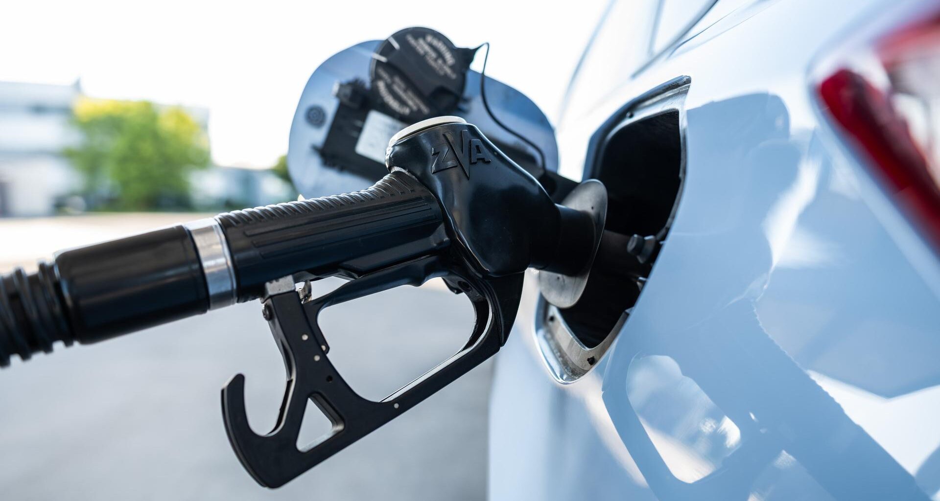 Ein Tankrüssel steckt während eines Tankvorgangs in einem Verbrenner an einer Zapfsäule einer Tankstelle.