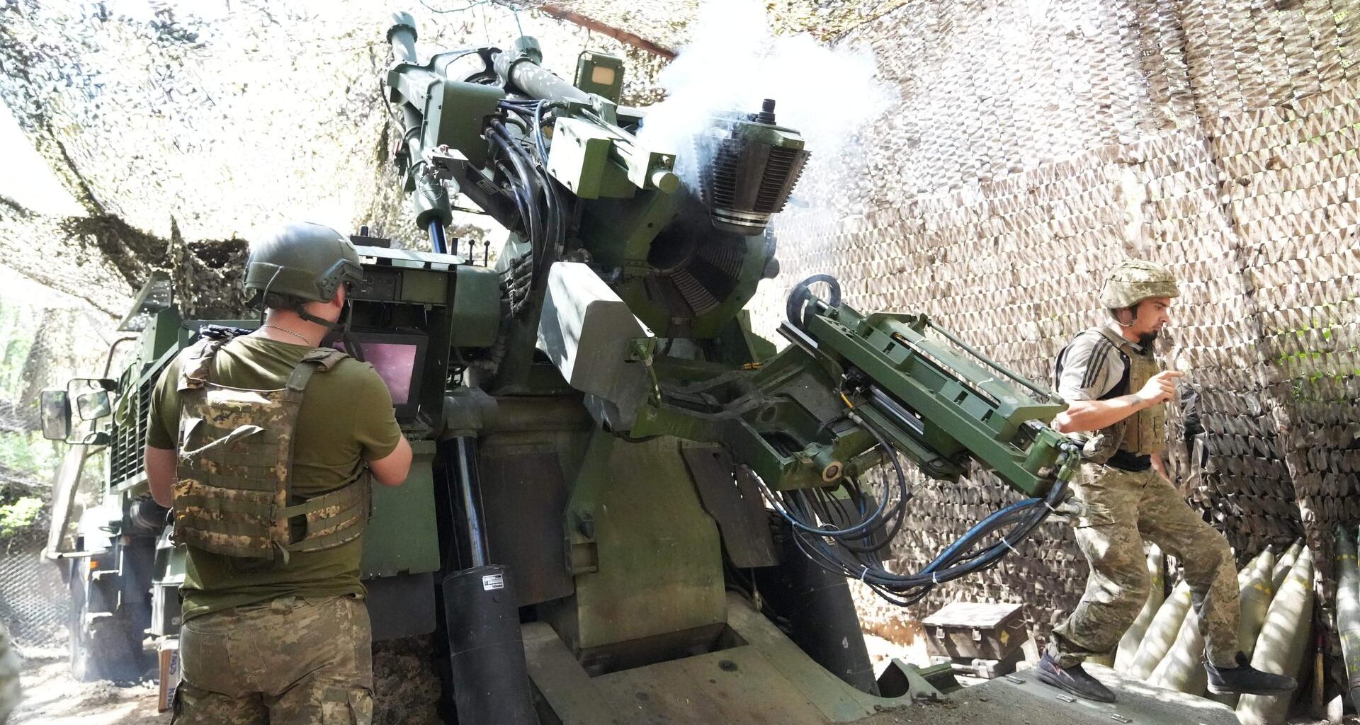 Soldaten feuern ein Artilleriegeschütz in einer getarnten Deckung ab.