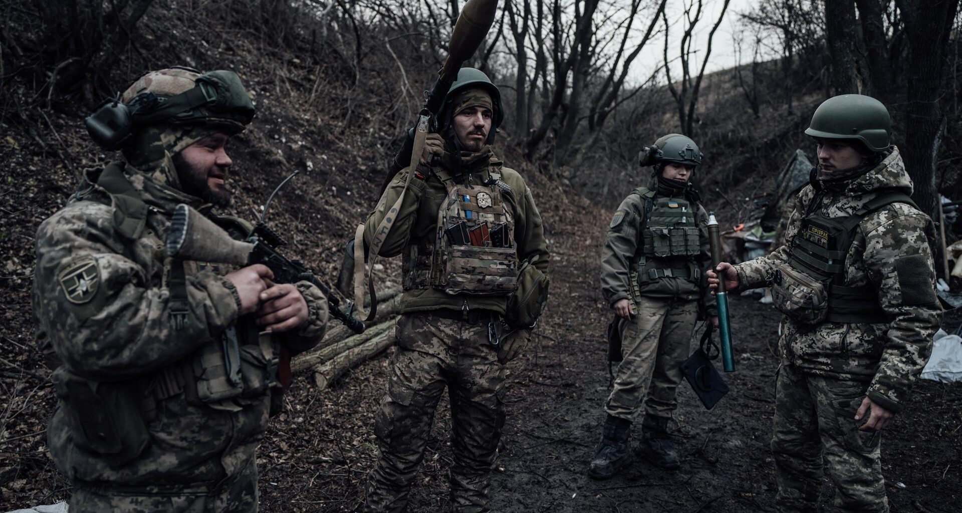 Vier Soldaten im Donbass stehen in einem Waldstück nebeneinander mit Artillerie. Im hinterrgrund sieht man eine Art Zelt. Copyright Adrien Vautier. März 2023.