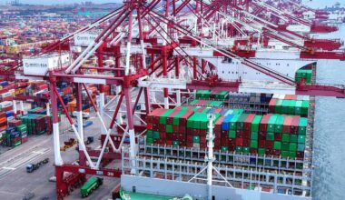Lastwagen fahren an einem Schiff vorbei, das an einem Containerterminal in der ostchinesischen Provinz Shandong angedockt ist
