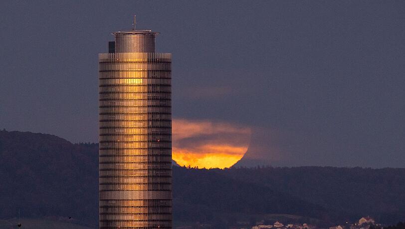Der Vollmond geht hinter dem Business Tower Nürnberg auf. Gleichzeitig taucht die untergehende Sonne den Turm in ein orangefarbenes Licht.