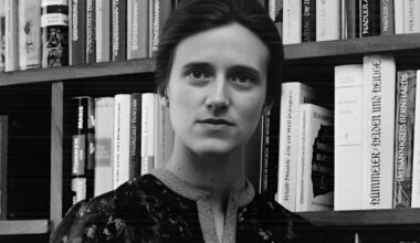 Erentraud Müller - Schwarz-weißes Foto von Erentraud Müller als junge Frau, vor einem Bücherregal stehend, mit Buch in der Hand und Blick in die Kamera - © Otto Müller Verlag Salzburg