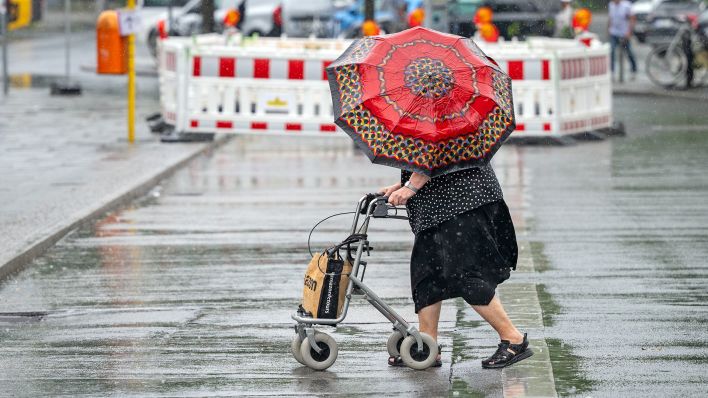 Eine Frau mit Rollator und Regenschirm geht am 15.07.2025 im Regen über den Berliner Hardenbergplatz. (Quelle: dpa-Bildfunk/Soeren Stache)