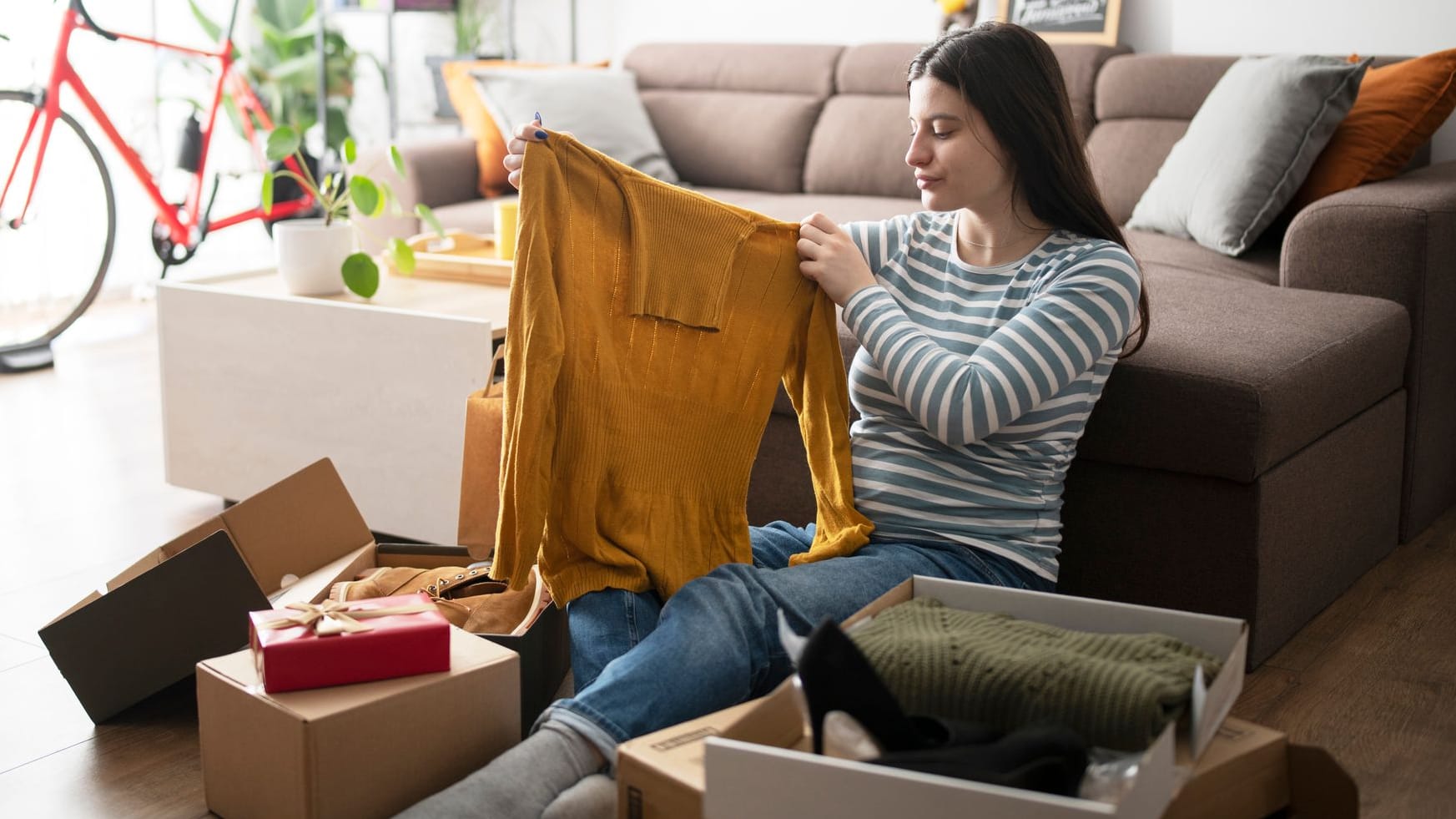 Junge Frau sitzt auf dem Fußboden und packt Pakete aus