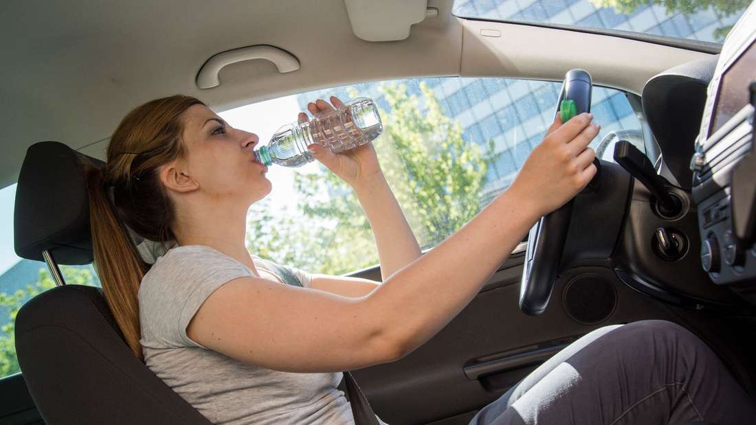 Frau trinkt während der Autofahrt aus einer Wasserflasche