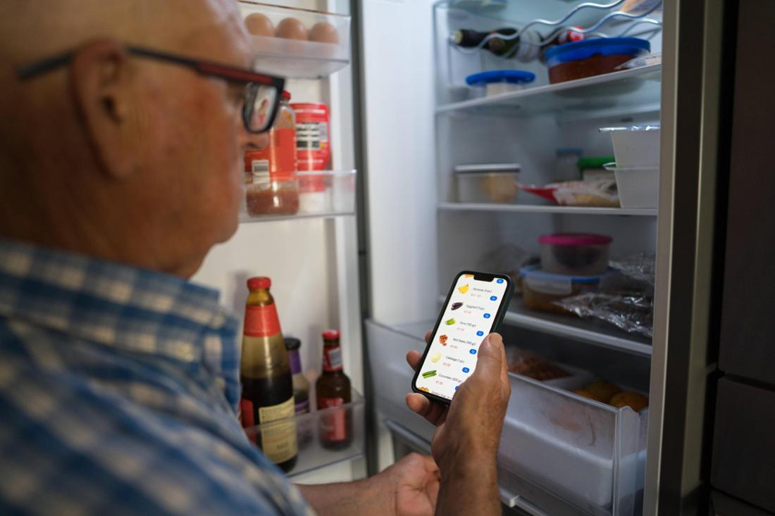 Ein älterer Mann nutzt via Smartphone seinen Smart-Home-Kühlschrank