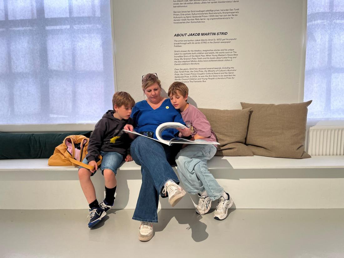 Besucher der Strid-Ausstellung im Kunstmuseum Brandts in Odense blättern durch das Buch „Der fantastische Bus“.