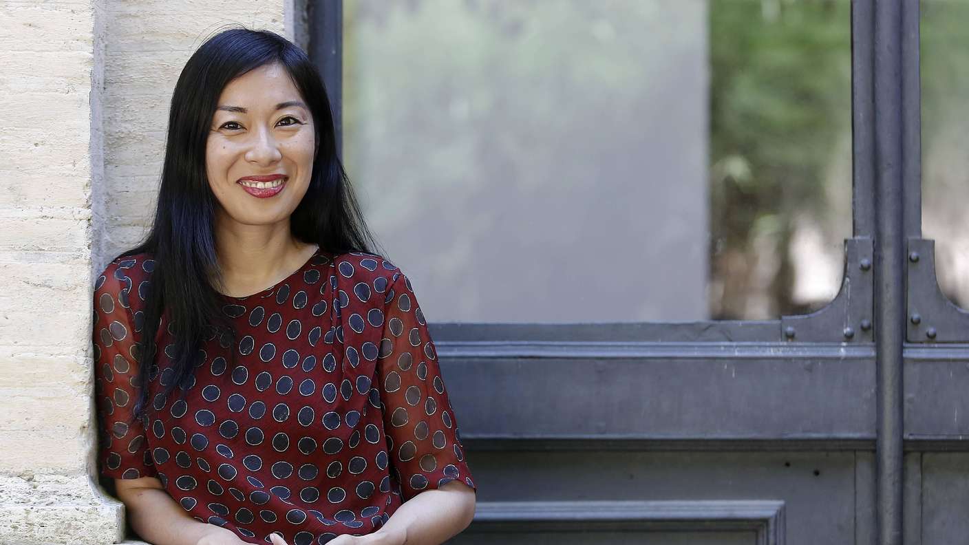 Katie Kitamura steht an einen Türeingang gelehnt und lächelt in die Kamera.