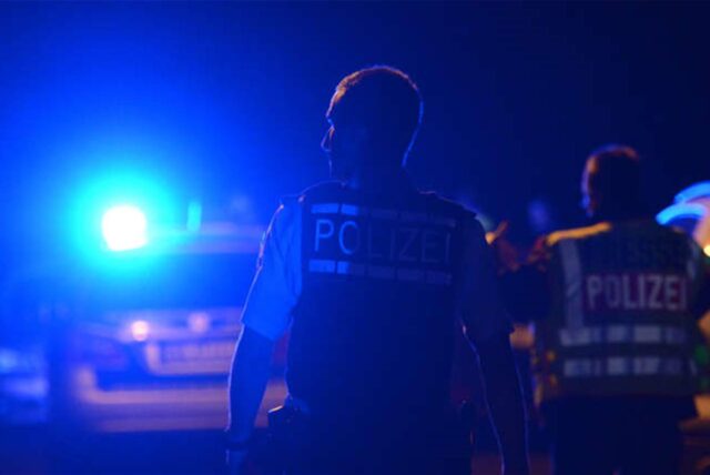 Polizisten stehen vor einem Polizeiauto mit dem Rücken zur Kamera. (Symbolbild)