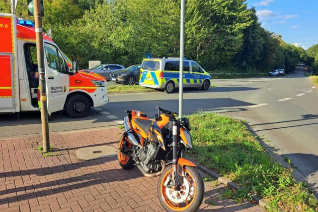 Nach einem Unfall steht ein beteiligtes Motorrad am Straßenrand, dahinter ein Notarztwagen und ein Einsatzfahrzeug der Polizei.