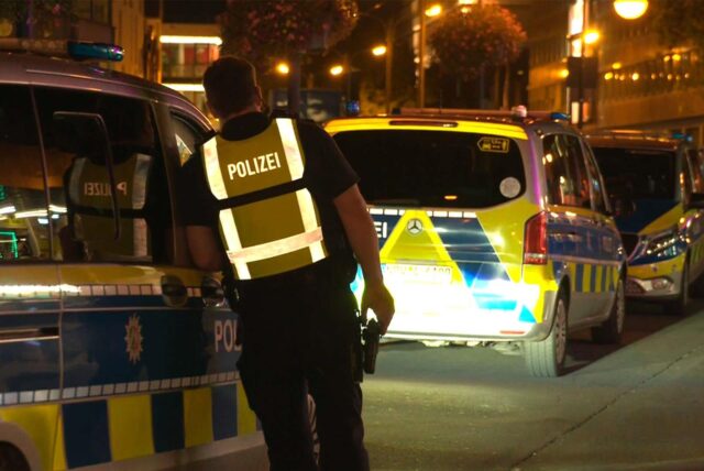 Ein Polizist lehnt auf der Kampstraße in der Dortmunder Innenstadt an ein Polizeiauto.