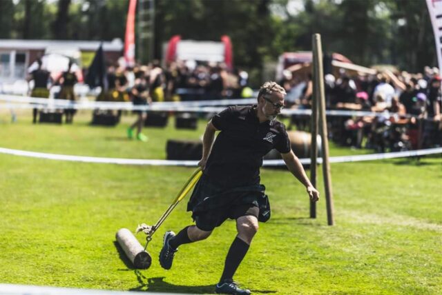 Ein Sportler, der bei Highland Games antritt, zieht einen Baumstamm hinter sich her.