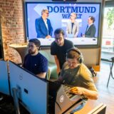 Auf einem großen Bildschirm ist zu sehen, wie zwei Journalisten den Oberbürgermeister von Dortmund, Thomas Westphal, interviewen. Davon sitzen, an einem Mischpult und vor mehreren Bildschirmen, Video-Techniker.