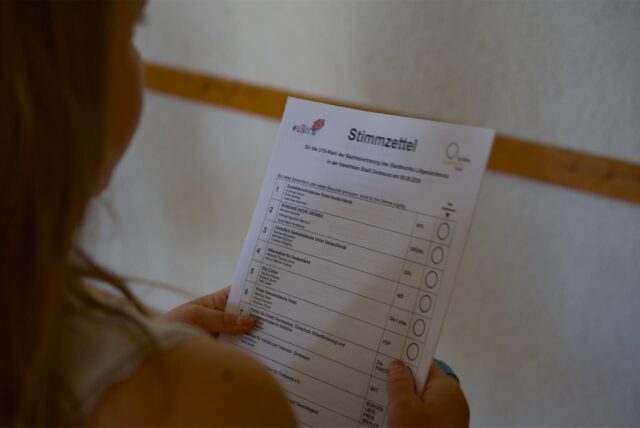 Ein Mädchen hält einen Wahlzettel in der Hand.