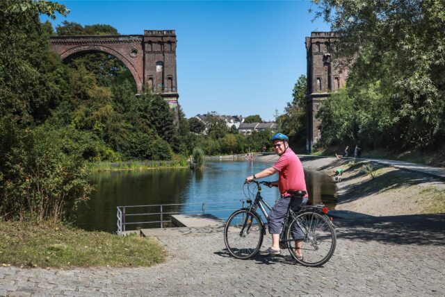 Reporter Oliver Volmerich sitzt auf dem Fahrrad vor dem alten Viadukt auf Phoenix-West in Dortmund.