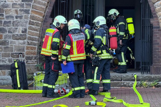 Feuerwehrleute stehen vor dem Portal der Christuskirche in Herten-Westerholt. Davor liegen Schläuche.