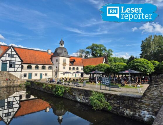 Ein Blick auf das Wasserschloss Haus Dahl in Bochum an einem sonnigen Tag. Im Außenbereich des Schlosses befindet sich ein Gastronomiebereich mit mehreren Gästen.