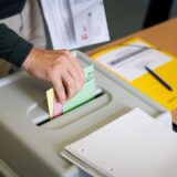 Eine Hand wirft die Wahlscheine ein.