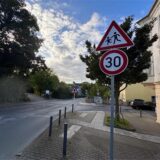 Ein Verkehrsschild mit der Aufschrift „30“ und einem Warnzeichen für Kinder befindet sich am Straßenrand. Die Geschwindigkeitsbegrenzung soll Verkehrsteilnehmer auf die mögliche Anwesenheit von spielenden Kindern hinweisen.
