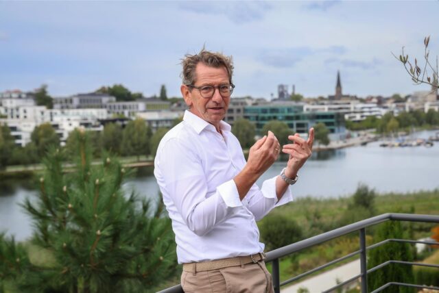 Galert steht auf der Dachterrasse und gestikuliert in die Kamera.