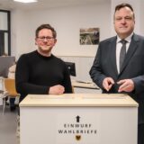 Wahlleiter Norbert Dahmen (r.) und Wahlbüro-Leiter Marc Rostohar mit der Briefwahlurne im städtischen Wahlbüro am Königswall.