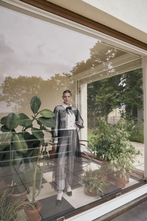 Chanel. Anna trägt Hose und Top aus weißem Tweed, darüber eine Bluse und einen Rock aus Tüll und dazu Lederstiefel.