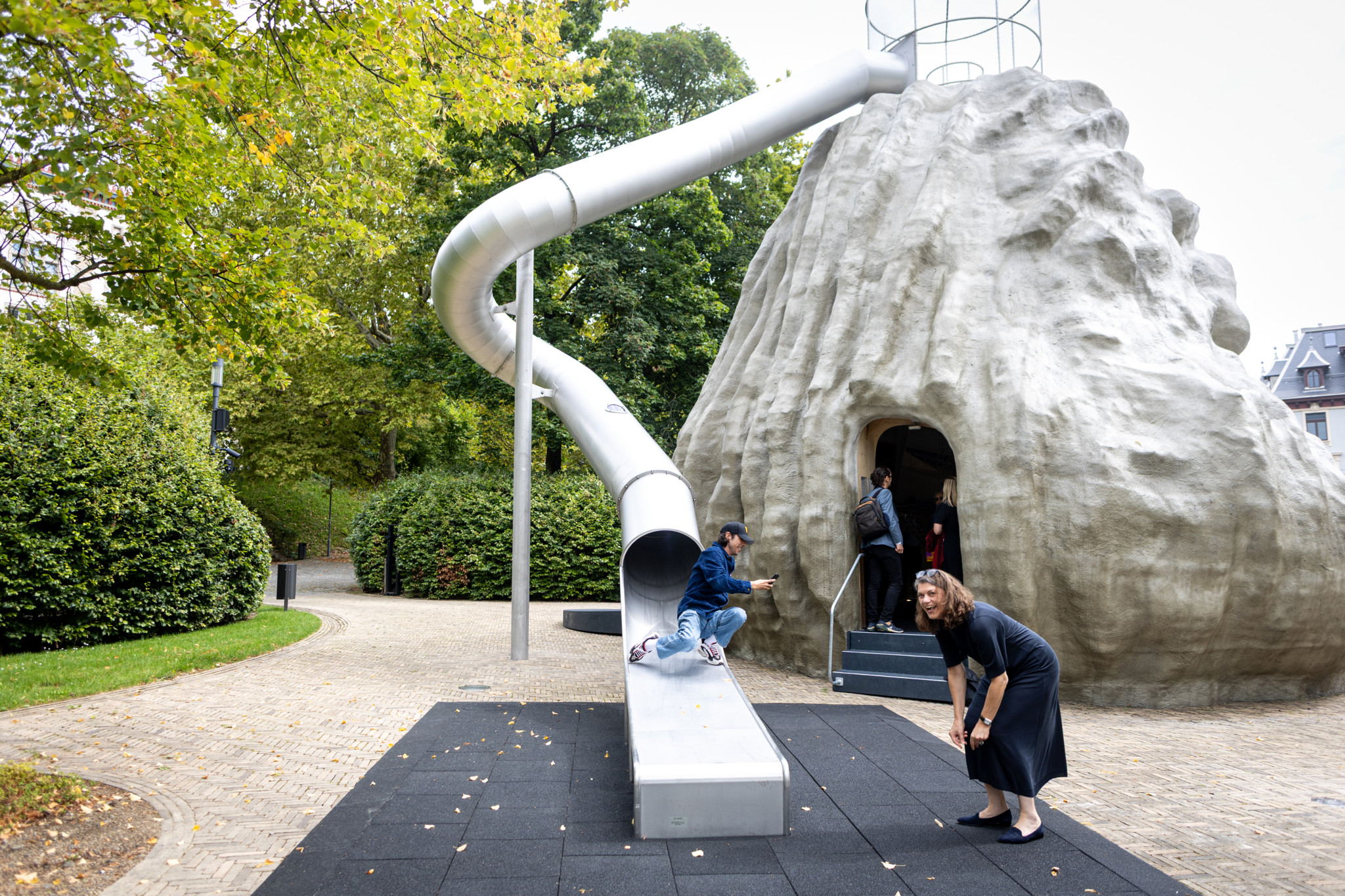 Begehbare Kunstskulptur von Monster Chetwynd im Park in Zürich, mit Klettergerüst und Rutsche, Menschen erkunden die Installation.