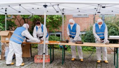 Menschen in Schutzanzügen stehen an einem Tisch