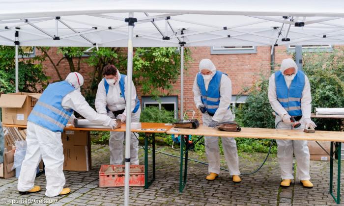 Menschen in Schutzanzügen stehen an einem Tisch