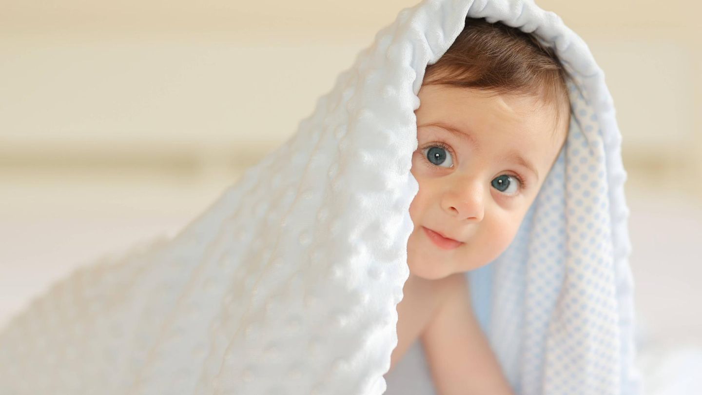 Abnehmspritzen können Kinderwunsch erfüllen: Ein Baby krabbelt unter einer weißen Decke hervor