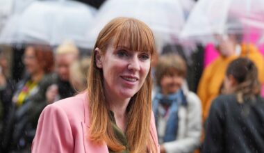 Angela Rayner lächelt in die Kamera. Hinter ihr sieht man verschwommen Menschen, die Regenschirme halten.