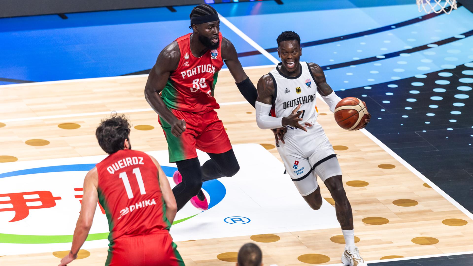 Basketballer Dennis Schröder dribbelt mit dem Ball und wird von einem Gegenspieler verfolgt.