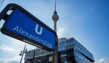 Aufnahme des U-Bahn Schildes am Bahnhof Alexanderplatz. Im Hintergrund ist vor blauem Himmel auch der Fernsehturm zu sehen.