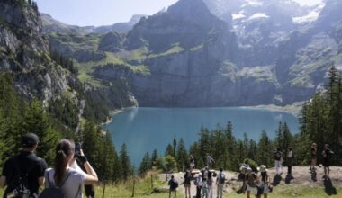 Auswanderziel: Wiese, Blauer Himmel, schneebedeckte Gipfellandschaft in der Schweiz, Wanderer vor Bergsee