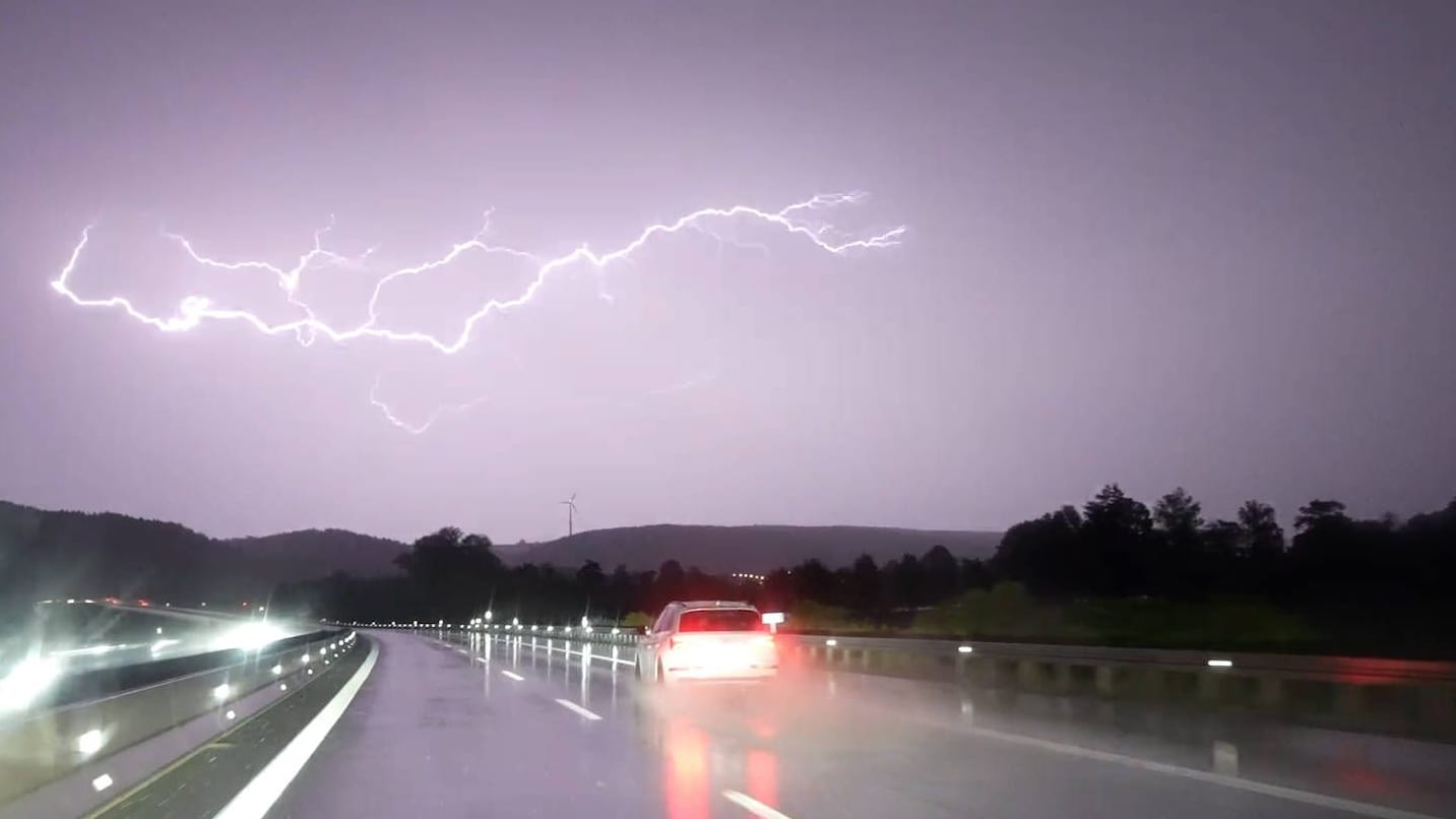 Blitze am Himmel über einer Landstraße (Symbolbild): Der Deutsche Wetterdienst rechnet in Köln und NRW ab Montag mit Unwettern und Sturmböen.