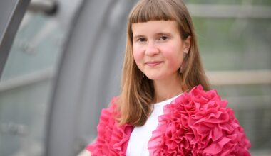 Eine junge Frau mit ungewöhnlicher Pnyfrisur und einer pinken Jacke schaut in die Kamera: die Schriftstellerin Caroline Wahl