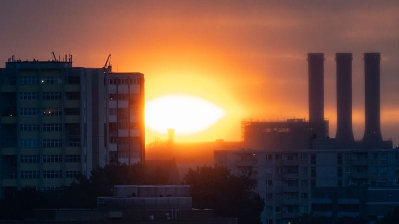 Die Sonne geht hinter Gebäuden und dem Heizkraftwerk Charlottenburg unter (Archivbild): Bei Höchsttemperaturen zwischen 20 und 23 Grad ist mit einem stark bewölkten Himmel in Berlin und Brandenburg zu rechnen.