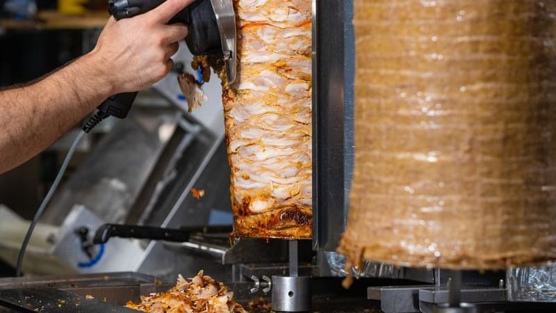 Ein Mitarbeiter einer Dönerbude schneidet Fleisch von einem Dönerspieß.