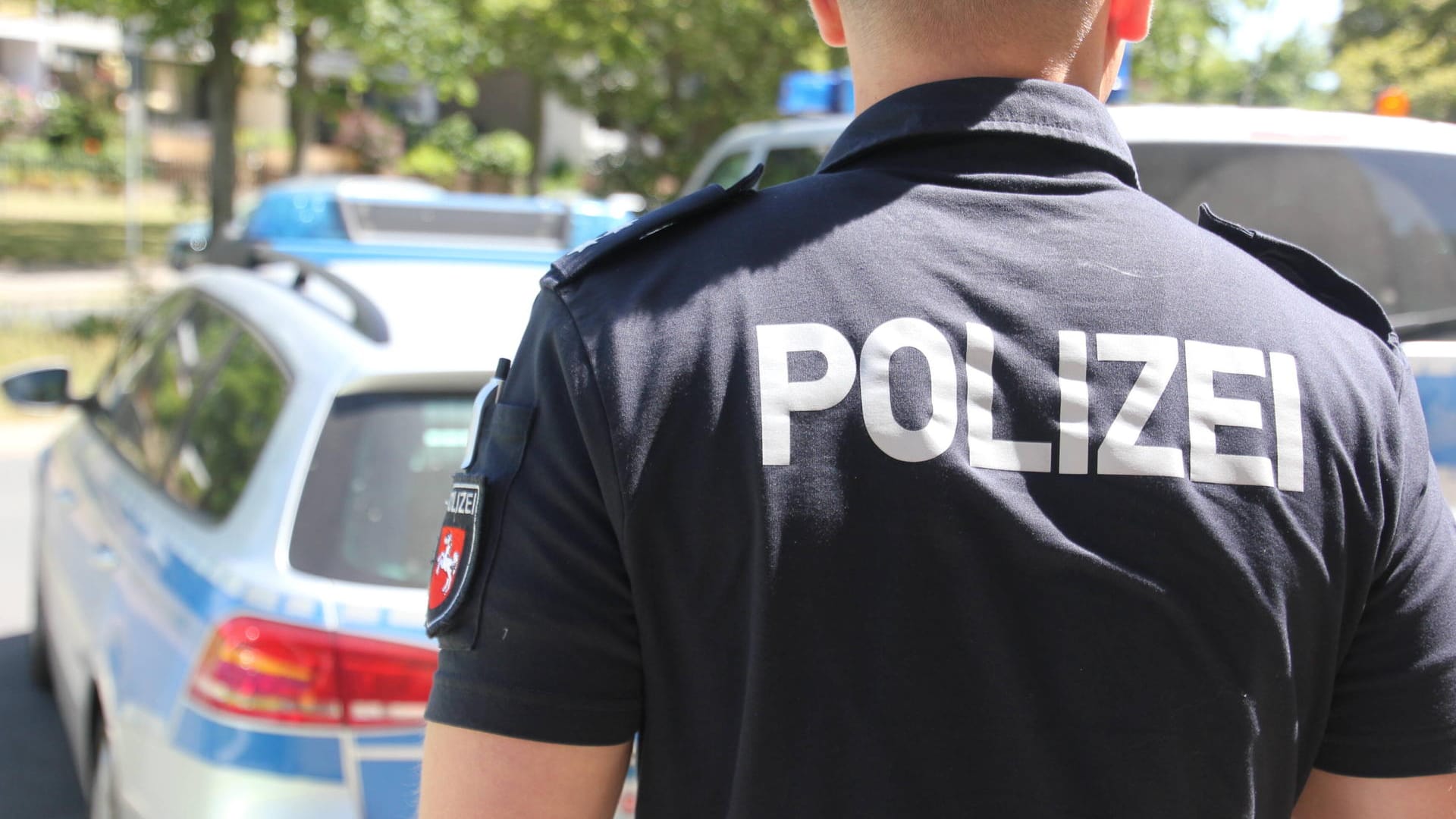 Ein Polizeibeamter steht vor einem Einsatzwagen (Symbolbild): Nach einem Überfall auf einen Wolfsburger sucht die Polizei nach Zeugen.