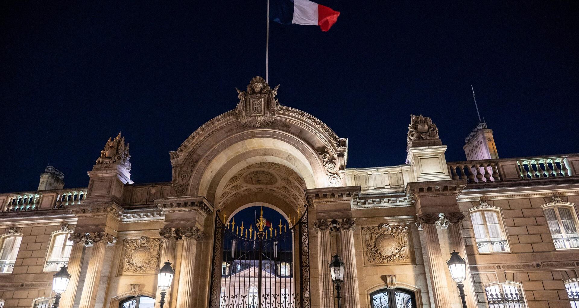 Über dem erleuchteten Elysee-Palast in Paris weht in der Dunkelheit eine Frankreich-Fahne.