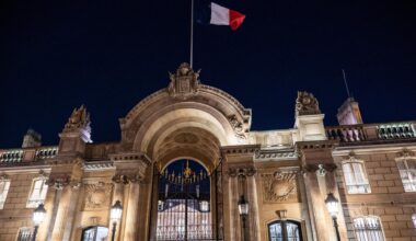 Über dem erleuchteten Elysee-Palast in Paris weht in der Dunkelheit eine Frankreich-Fahne.