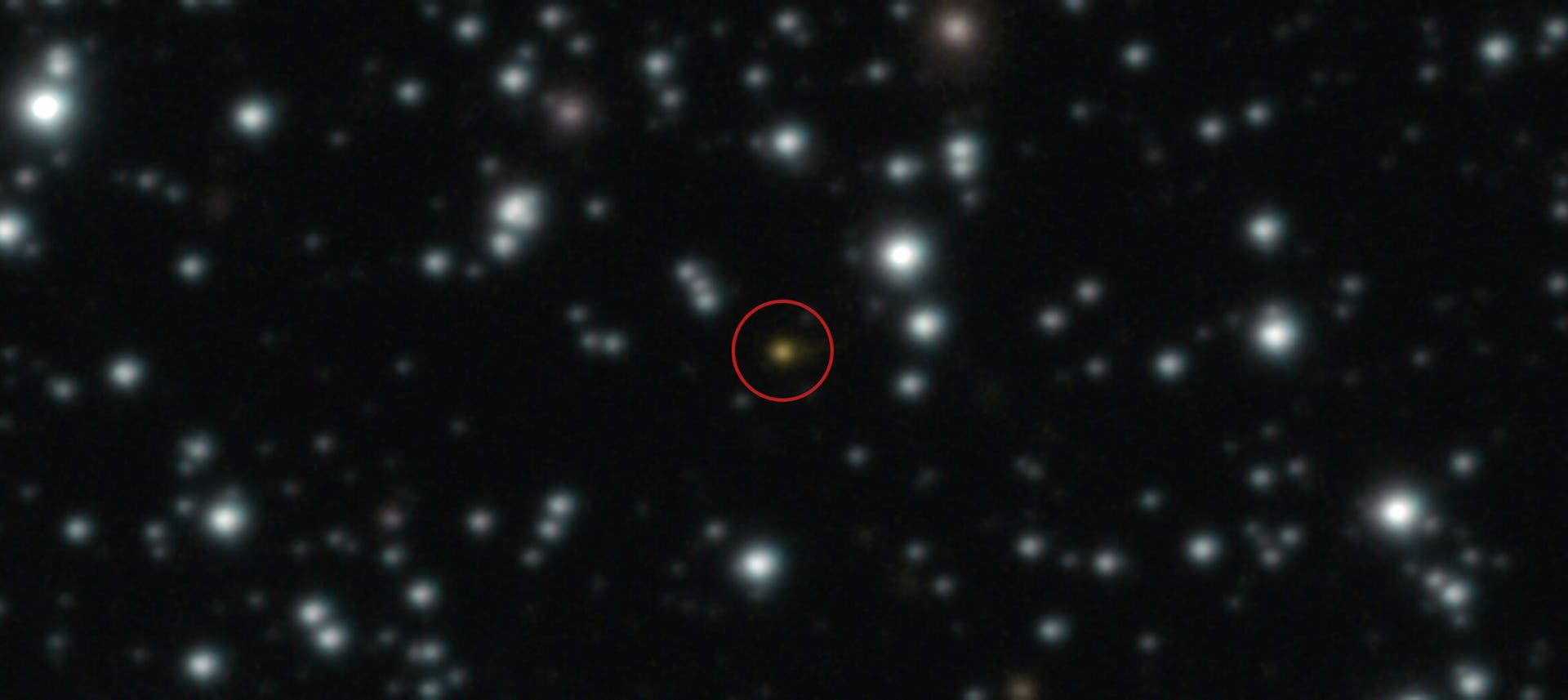 Ein astronomisches Bild zeigt einen Sternenhimmel mit zahlreichen leuchtenden Punkten vor einem dunklen Hintergrund. Ein Objekt in der Mitte ist rot eingekreist, um es hervorzuheben.