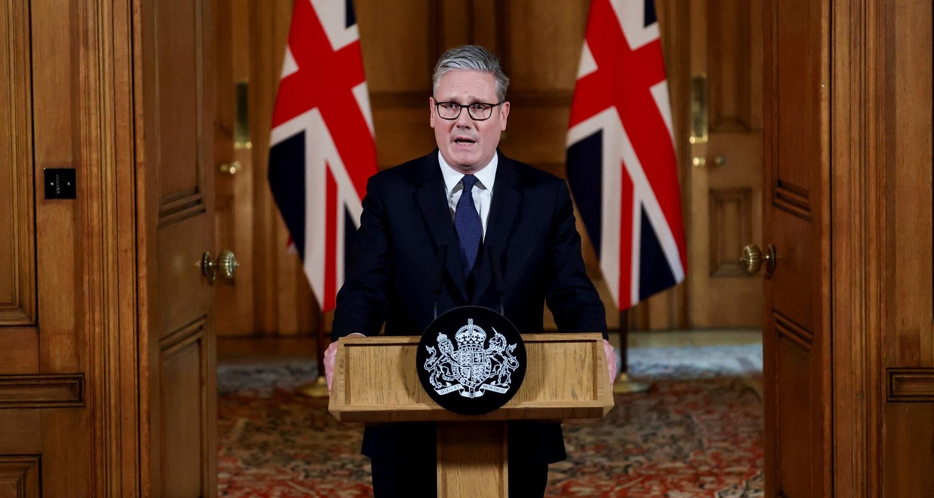 Der britische Premierminister Starmer steht hinter einem Rednerpult, hinter ihm zwei Landesflaggen.