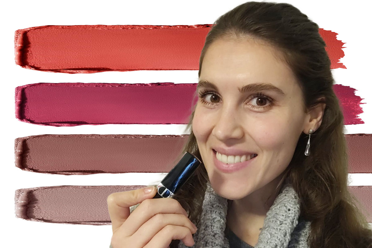Eine Frau mit langen dunklen Haaren hält sich einen Lippenstift vors Gesicht. Im Hintergrund Streifen von Lippenstift in unterschiedlichen Farben