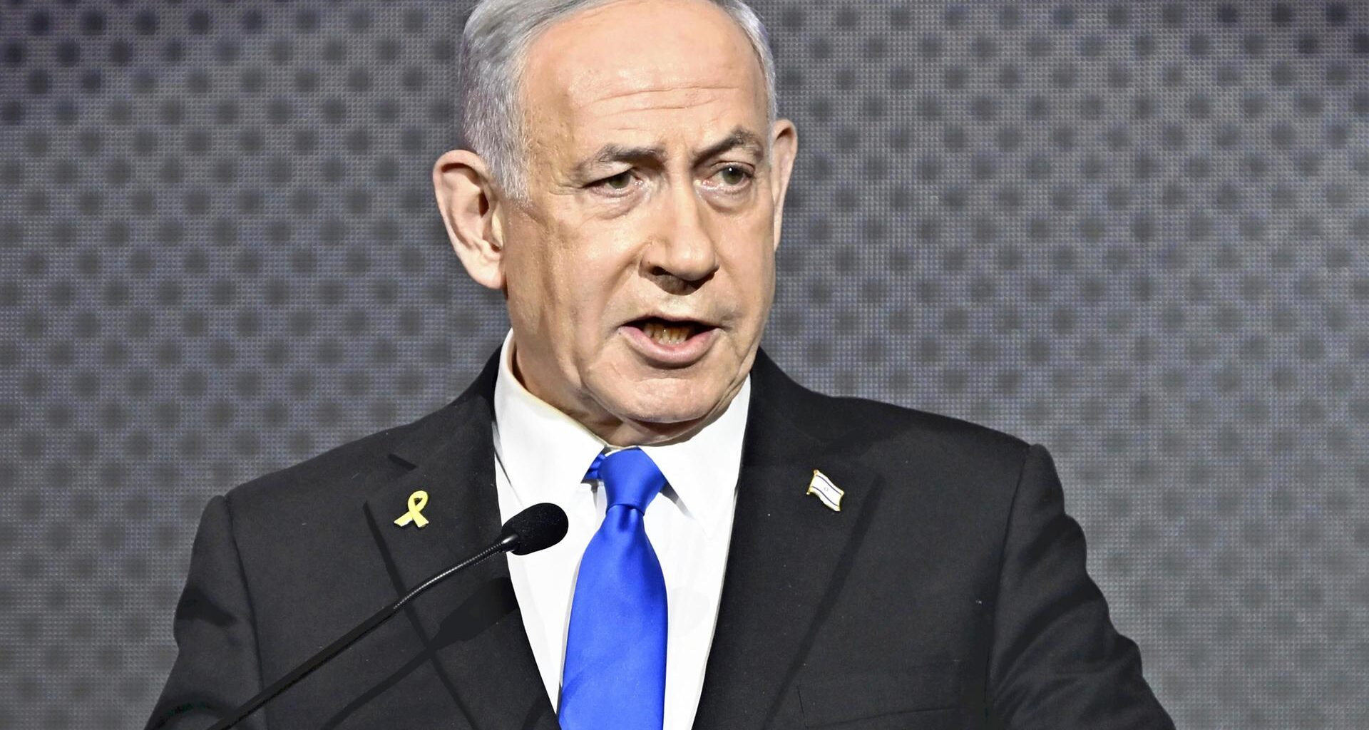 Der israelische Ministerpräsident Benjamin Netanjahu spricht im Anzug vor dunkelgrauem Hintergrund an einem Podium.